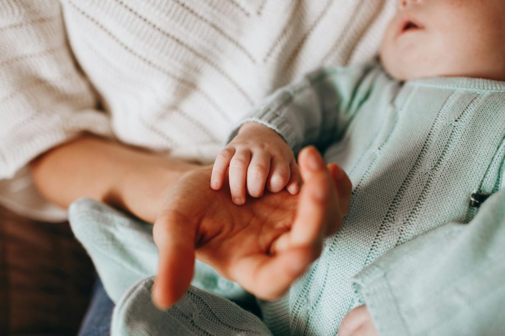 Gros plan intime d'une mère tenant la main de son bébé, soulignant un moment tendre.